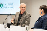 Bildbeschreibung: Ein Mann steht in einem Konferenzraum an einem Podium und spricht, im Hintergrund Logo 'Land Steiermark'.