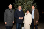 Eine Frau und drei Männer stehen vor einem festlich beleuchteten Weihnachtsbaum. Es ist eine stimmungsvolle Szene.