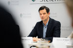 Person in formeller Kleidung spricht während eines Meetings. Im Hintergrund das Logo der Landesregierung Steiermark.