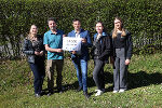 Gruppe von fünf Personen steht auf einer Wiese. Sie halten ein Schild mit der Aufschrift "8.500 gerettete Amphibien" hoch.