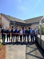 Gruppe von Personen schneidet ein rotes Band vor einem modernen Gebäude durch.