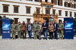 Bildbeschreibung: Gruppe in Militäruniform und zivilen Kleidungsstücken posiert vor einem Schloss mit dem Logo "Licht ins Dunkel".