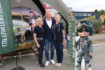 Drei Personen stehen vor einem Flugzeug-Display und einem Banner mit Höhenangaben. Im Hintergrund ein Festivalzelt.