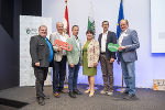 Gruppe von Menschen bei einem Event, halten Schilder mit Aufschriften hoch. Im Hintergrund Banner mit dem Steiermark-Logo.