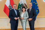 Drei Personen stehen nebeneinander vor den Fahnen der Steiermark, Österreichs und der EU.