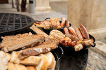 Grillgut, bestehend aus Fleisch, Wurst und Brot, auf einem Grillrost und in einer Pfanne.