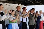 Gruppe von Menschen applaudiert bei einer Veranstaltung im Freien. Vielfältige Kleidung und Geschlechter sind erkennbar.