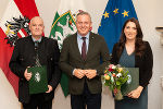 Bildbeschreibung: Drei Personen stehen vor Flaggen. Sie halten Dokumente und Blumen. Ein förmliches Porträt aus einem politischen Kontext. #Steiermark #Politik